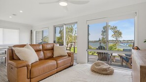Ein modernes Wohnzimmer mit einem Ledersofa, einem kleinen Sitzsack und Seeblick durch große Fenster.