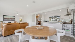 A modern kitchen with white cabinetry, a dining table with white chairs, and a brown leather sofa. - Shoreline Shack - Escape to the peaceful North Shore of Port Macquarie (North Shore)
