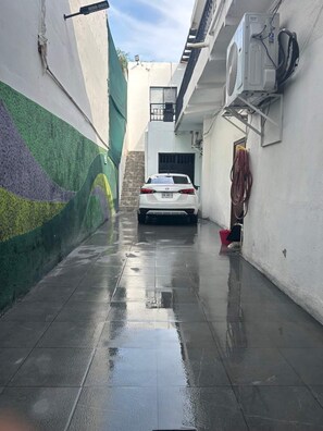 A narrow alleyway with a white car parked in the center, a green wall on the left, and an air conditioning unit on the right. - Casa Arteaga (Monterrey)