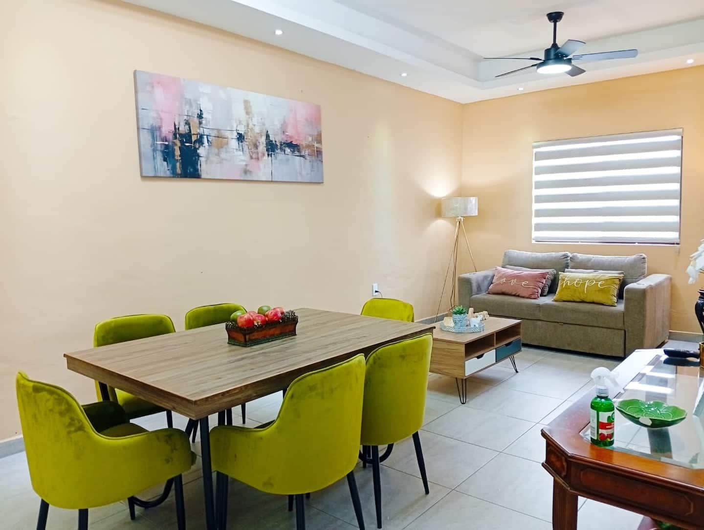A dining area with a wooden table and yellow chairs, a sofa with cushions, and a painting on the wall.