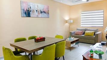 A dining area with a wooden table and yellow chairs, a sofa with cushions, and a painting on the wall.