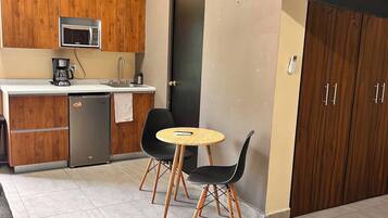 A compact kitchen with a microwave, coffee maker, and a small refrigerator. There is a dining area with two chairs and a small round table.