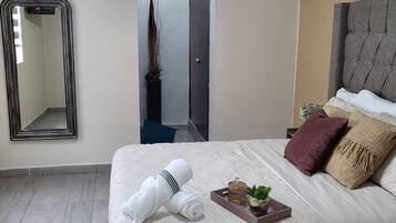 A hotel room with a bed, a mirror, a door, and a small plant.