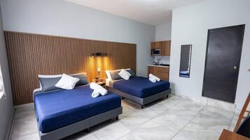 Habitación de hotel con dos camas, cabecera de madera, kitchenette pequeña y una puerta.