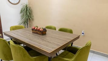 Une salle de conférence avec une table en bois, des chaises vertes, une horloge, une plante et un tableau accroché au mur.