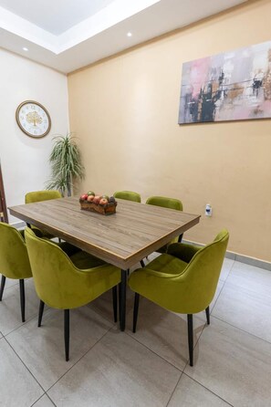 A conference room with a wooden table, green chairs, a clock, a plant, and a painting on the wall. - Casa Arteaga (Monterrey)