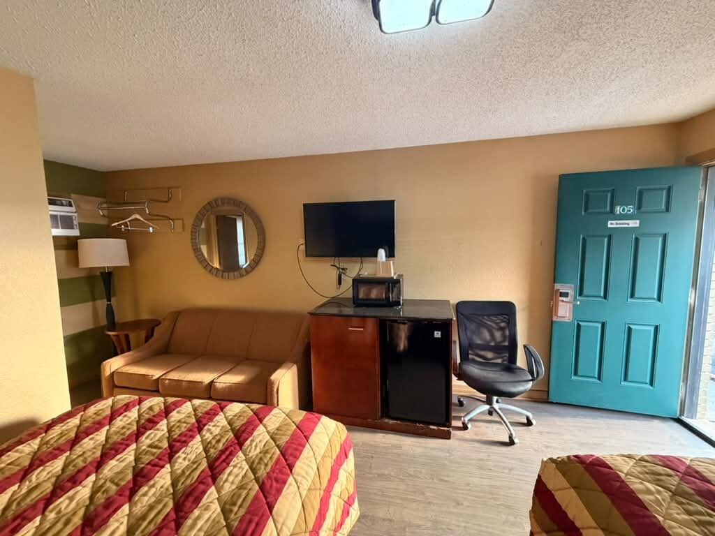 Habitación de hotel con dos camas, un escritorio con computadora, una silla, un televisor, una puerta y una ventana.
