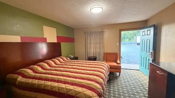 A hotel room with a large bed, a chair, a desk, and a view of the outside.