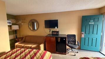 A hotel room with two beds, a desk with a computer, a chair, a TV, a door, and a window.
