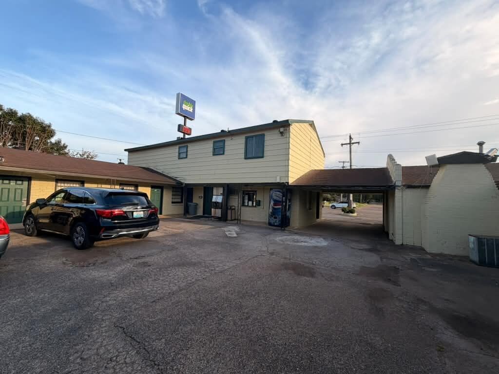 Un motel con estacionamiento, un automóvil y un letrero.