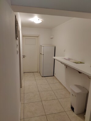 A narrow hallway with a white door, a white refrigerator, a white trash bin, and a white shelf with a book. - Art apartment Syngrou - 5 min walk to Acropolis (Athina)