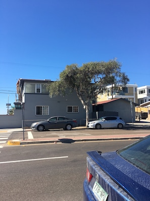 A street view with a blue car parked on the side, a tree, and buildings in the background. - MISSION BEACH 1-bedroom w/ Large Ocean View Deck 714 (San Diego)
