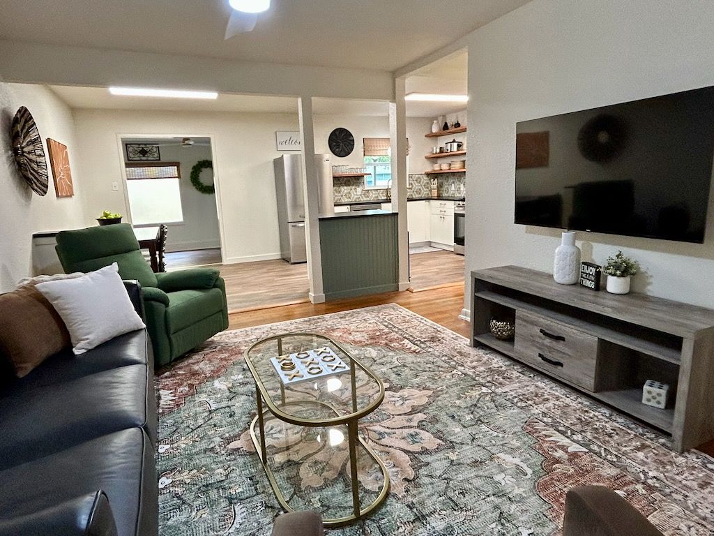 Una sala de estar con un sofá, una mesa de centro y un televisor. Se observa una cocina al fondo.