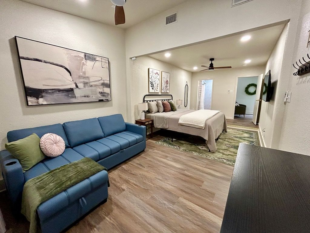 Ein Schlafzimmer mit einem blauen Sofa, einem Bett mit weißer Bettdecke und einem Deckenventilator.