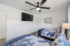 Ein Hotelzimmer mit Deckenventilator, einem Flachbildfernseher, zwei Betten mit passender blau-weißer Bettwäsche, einem kleinen Gemälde an der Wand und einer Nachttischlampe.