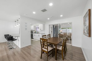 Eine moderne Küche mit weißen Schränken und einem Essbereich mit einem Holztisch und Stühlen.