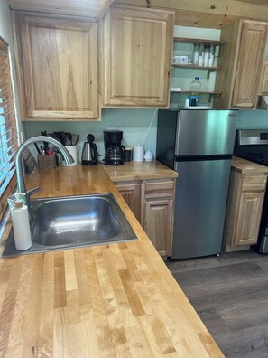 A kitchen with wooden cabinets, a stainless steel sink, a coffee maker, and a refrigerator. - Tranquil Tinyhouse in lovely forest 12min from downtown Sequim. Trees and deer (Sequim)