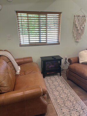 Un salon avec deux canapés en cuir marron, un tapis à motifs, une petite table noire avec un plateau en verre et une décoration murale en macramé.