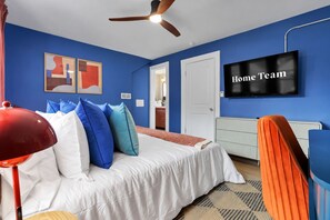 Ein Schlafzimmer mit einem Bett, einer roten Lampe, einem blauen Stuhl, einem Fernseher und einem Deckenventilator.