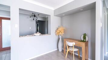 Un interior moderno con una consola de madera, una silla blanca, un espejo decorativo y un jarrón con plumas de pájaro.