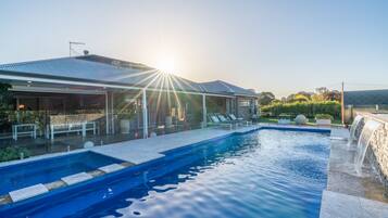 Ein Pool mit Wasserfall, eine überdachte Terrasse und ein Backsteinhaus mit Metallbedachung.