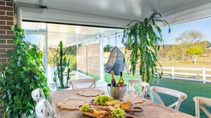 An outdoor dining area with a table set for a meal, surrounded by potted plants and a hanging chair. - Hillside Residence ~ Picturesque mountain views with four spacious bedrooms (Nowra Hill)