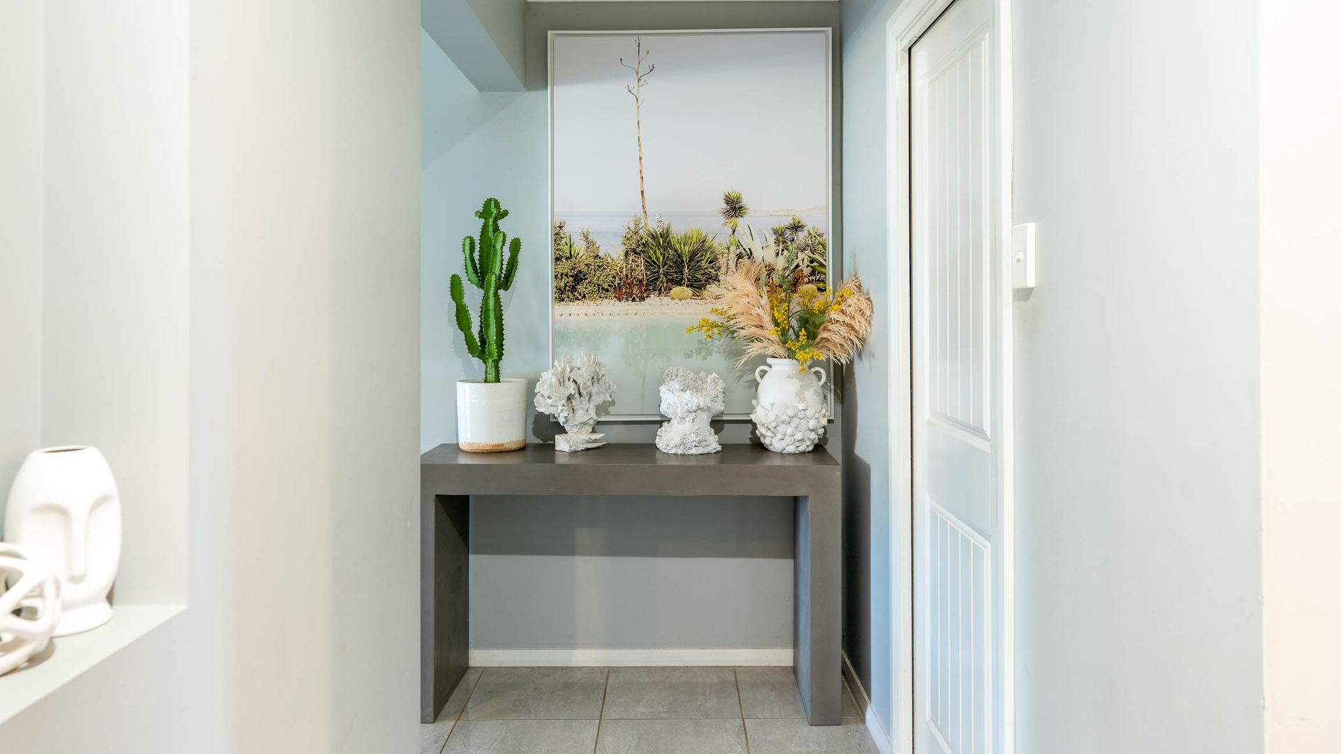 A hallway with a grey console table, a cactus, and decorative rocks.