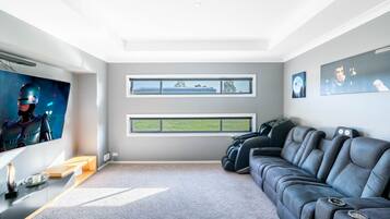 Un salon moderne doté d’un grand téléviseur à écran plat, d’un canapé gris et de deux fenêtres donnant sur un immeuble et sur la verdure.