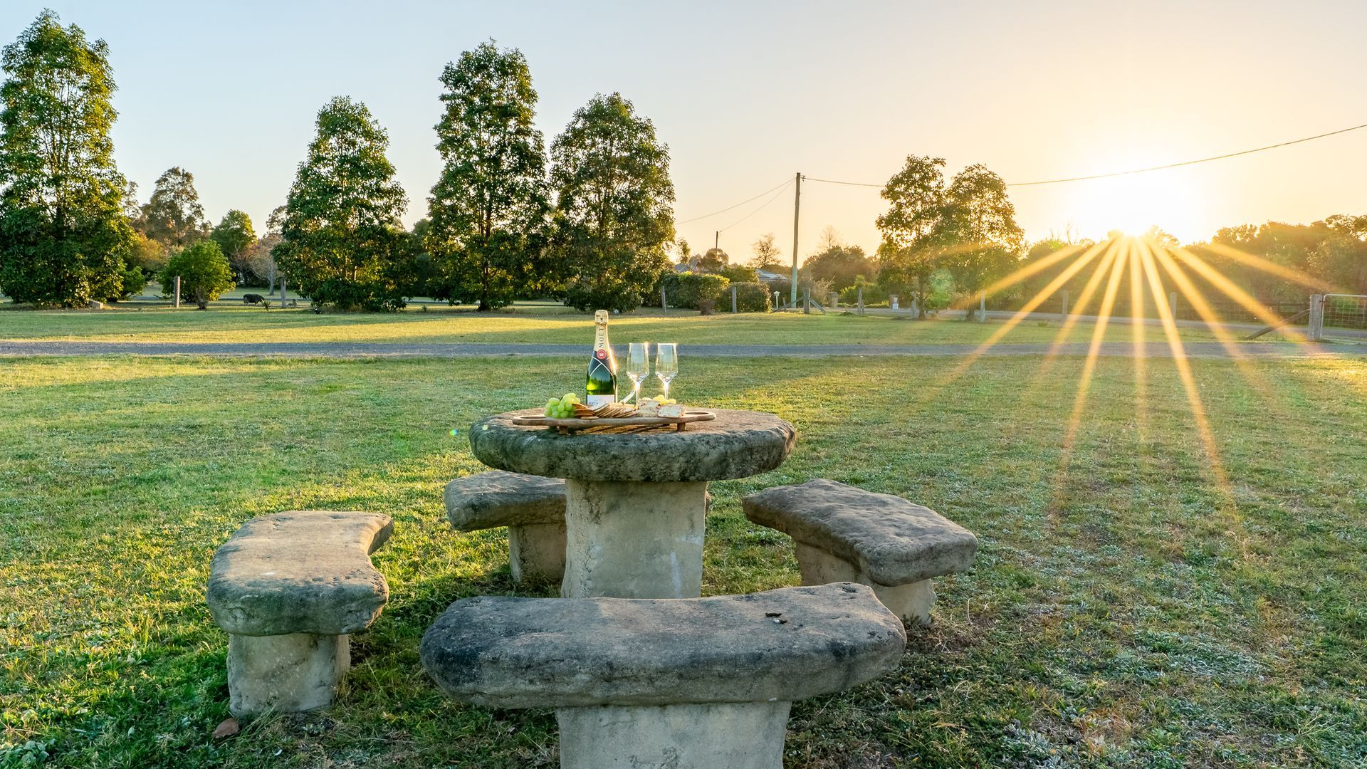 A picnic setup with a stone table and benches in a grassy park during sunset.
