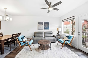 Uma sala de estar moderna com ventilador de teto, mesa de jantar com cadeiras, sofá e mesa de centro.