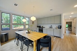 Eine moderne Küche mit einem Holztisch, schwarzen Stühlen und Blick auf den Wald durch große Fenster.