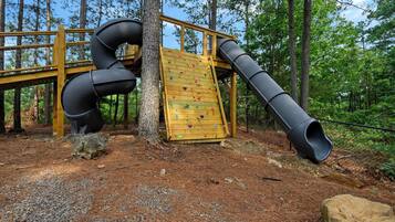 Ein Spielplatz mit Rutsche, Kletterwand und einer Holzterrasse.