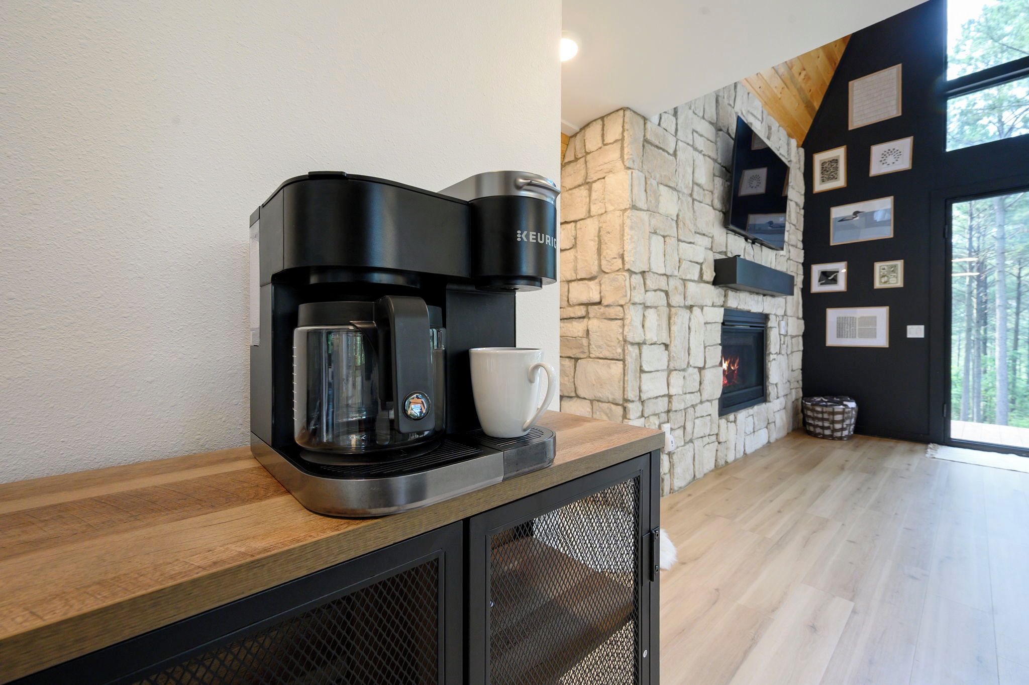 A modern kitchen with a Keurig coffee maker, a white mug, and a stone wall.