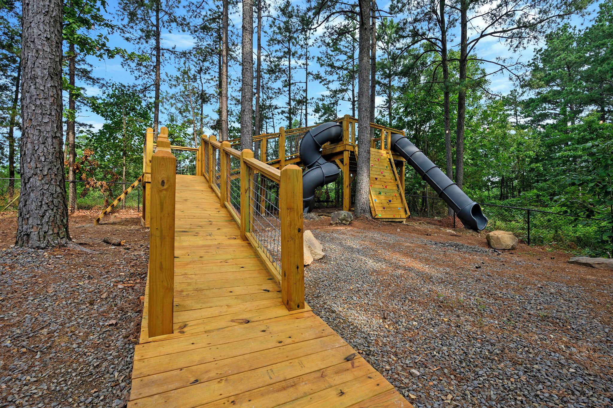 A wooden bridge leading to a playground with climbing walls and a slide.