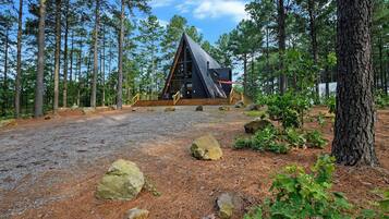 Eine Hütte mit einem dreieckigen Dach, umgeben von einem Wald mit Kiefern.