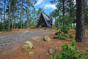 A cabin with a triangular roof, surrounded by a forest with pine trees. - Pine + Peak • Luxury A-Frame • Adventure Zone • Hot Tub (Broken Bow)