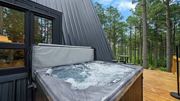 A hot tub on a wooden deck with a view of a forest.