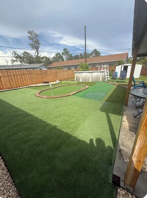 A backyard with artificial grass, a wooden fence, and a small shed. - 4-bedroom 5 bed pool & putt putt house with AC 5 minutes from St Pete (Pinellas Park)