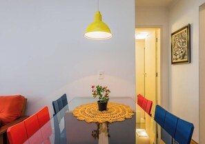 Ein Essbereich mit einem Glastisch, roten und blauen Stühlen, einer gelben Pendelleuchte und einem Blumentopf.