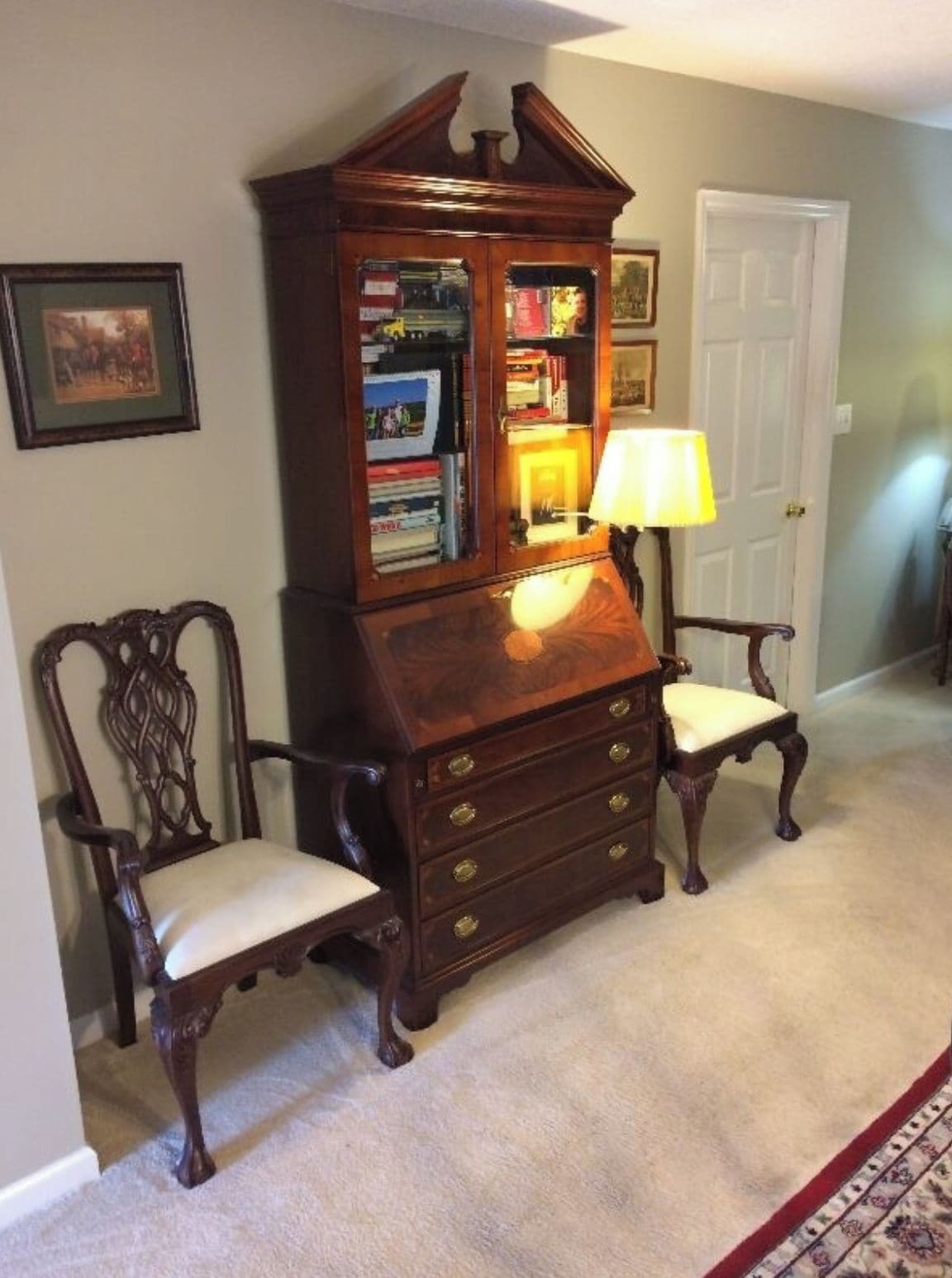 A hallway with a wooden bookcase, two chairs, a lamp, and a door.