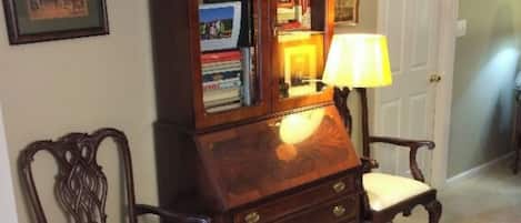 Un pasillo con una biblioteca de madera, dos sillas, una lámpara y una puerta.