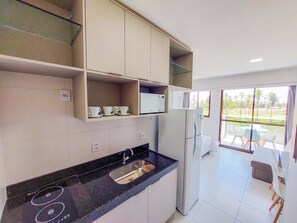 A modern kitchen with a black countertop, white cabinets, a built-in microwave, and a refrigerator. - Mana Beach Experience - Porto de Galinhas (Ipojuca)