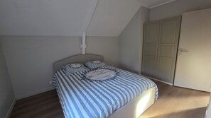 A bedroom with a bed, a wardrobe, and a sloped ceiling. - Apartment in the countryside near the ocean. (Quéven)