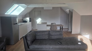 A compact living space with a kitchenette, a grey sofa, and a dining table. - Apartment in the countryside near the ocean. (Quéven)