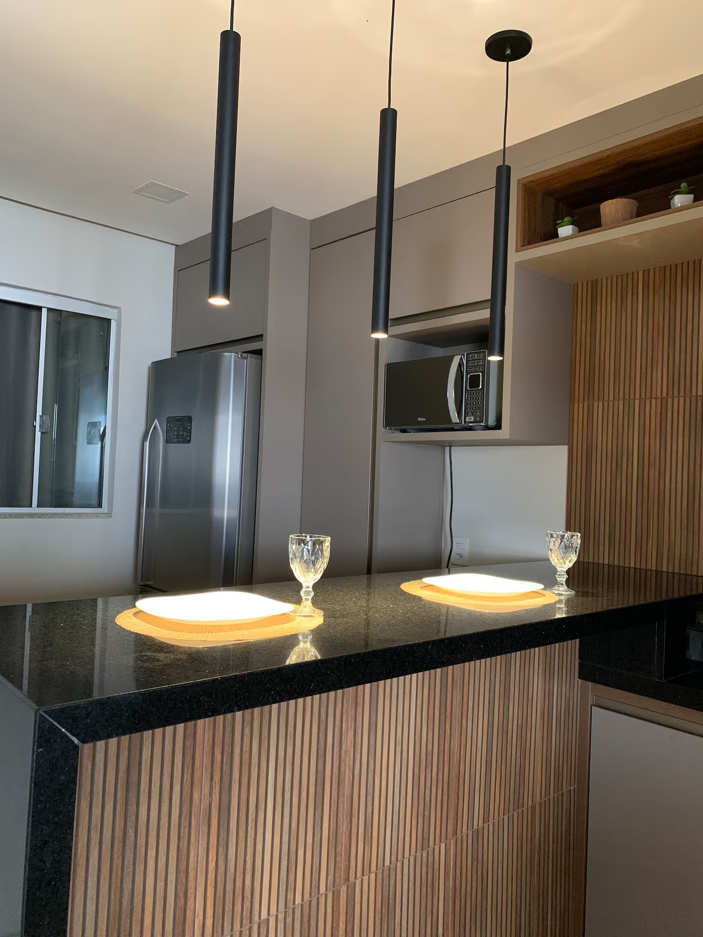 Une cuisine moderne dotée d’un plan de travail noir, d’appareils électroménagers en acier inoxydable et de luminaires suspendus.