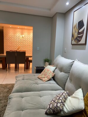 A modern living room with a sofa, pillows, a dining area, and a wall with a geometric pattern.