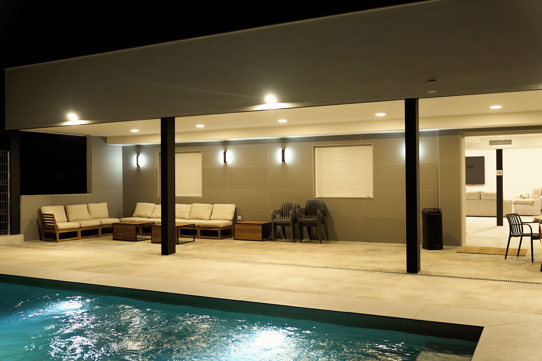 Un espace extérieur abrité comprenant une piscine, des sièges et une porte donnant accès à un espace intérieur.