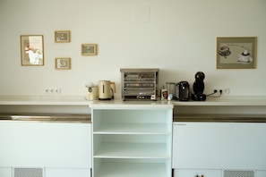 A kitchen with a coffee machine, a kettle, and a toaster on the counter. There are framed pictures on the wall.