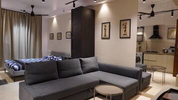 A modern living room with a grey sectional sofa, a small round table, and a bed with patterned bedding.