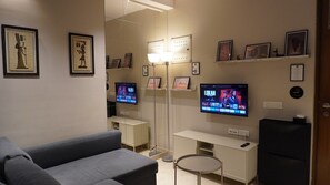 Ein modernes Wohnzimmer mit einem grauen Sofa, zwei Flachbildfernsehern, einer Stehlampe und gerahmten Bildern an den Wänden.